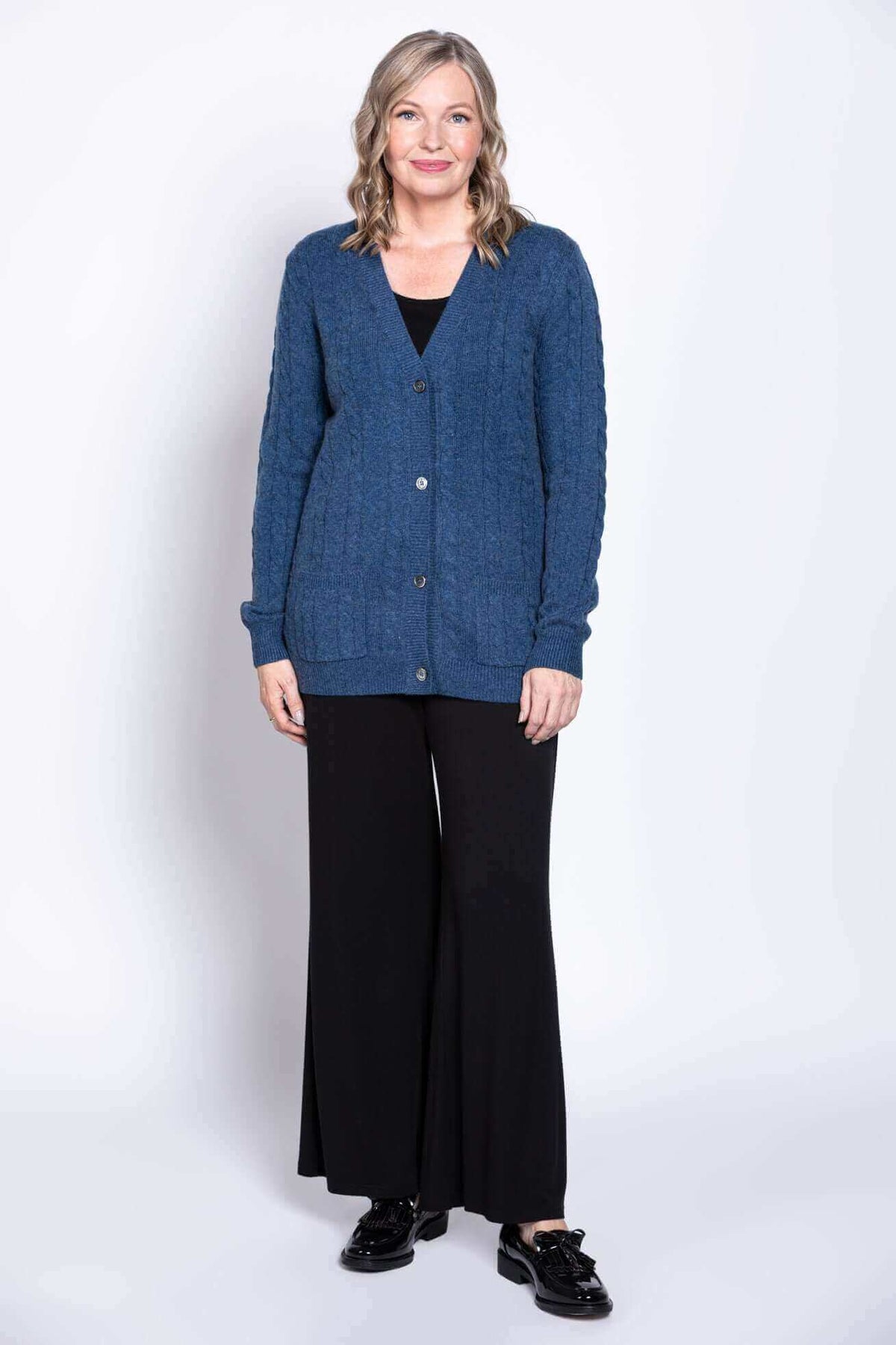 Woman standing in blue cable knit cardigan and wide-leg black pants