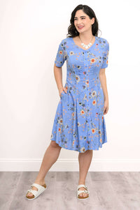 Model wearing a blue floral short sleeve dress with pockets and buttons, smiling