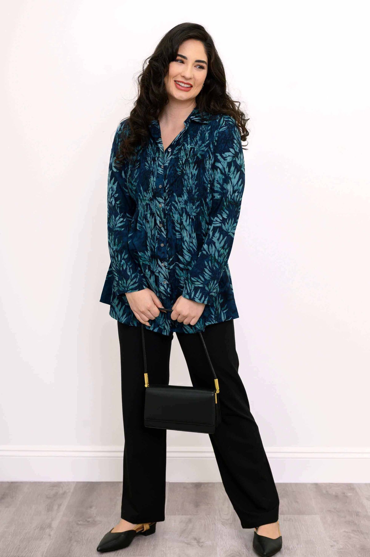 Model in blue smocked tunic holding a black handbag, smiling