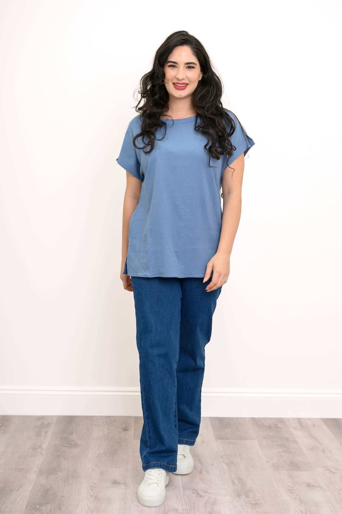 Full-body view of woman in blue tee and blue jeans with white sneakers