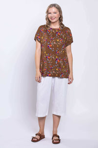 Woman smiling in brown floral linen tee and white pants, full outfit view