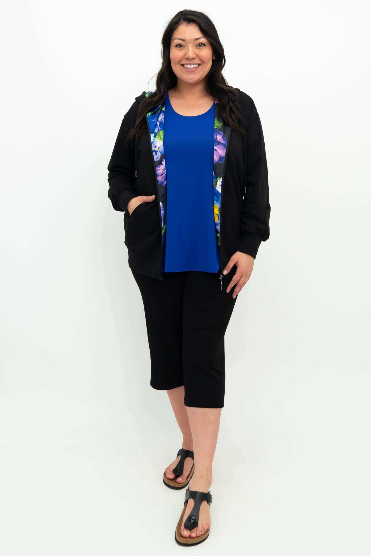 Full body view of model in black zip hoody, blue shirt, black capris, and sandals