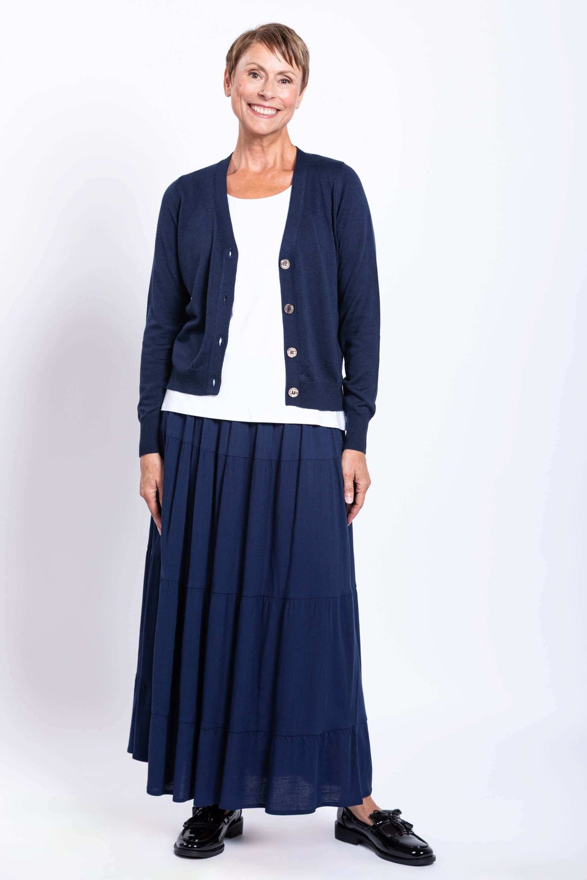 Full front view of model smiling in dark blue cardigan and matching skirt paired with a white top
