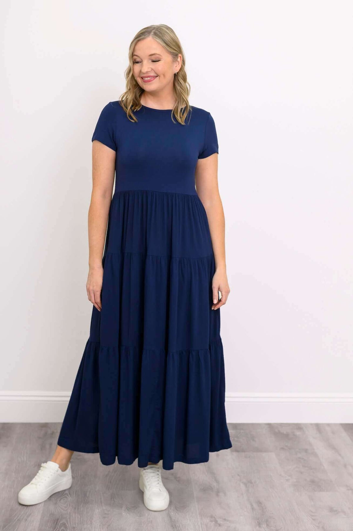 Model looking down in navy blue tiered maxi dress and white sneakers