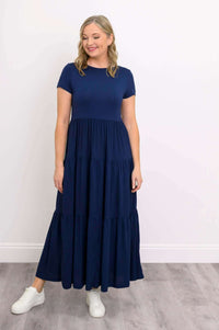 Model looking down in navy blue tiered maxi dress and white sneakers