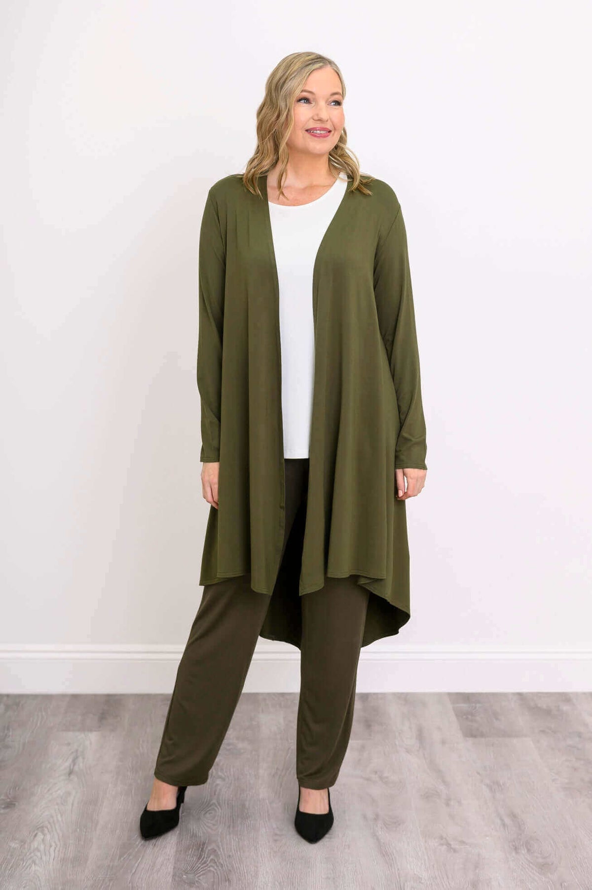 Model in olive green high-low duster, facing forward, hands relaxed, full outfit visible