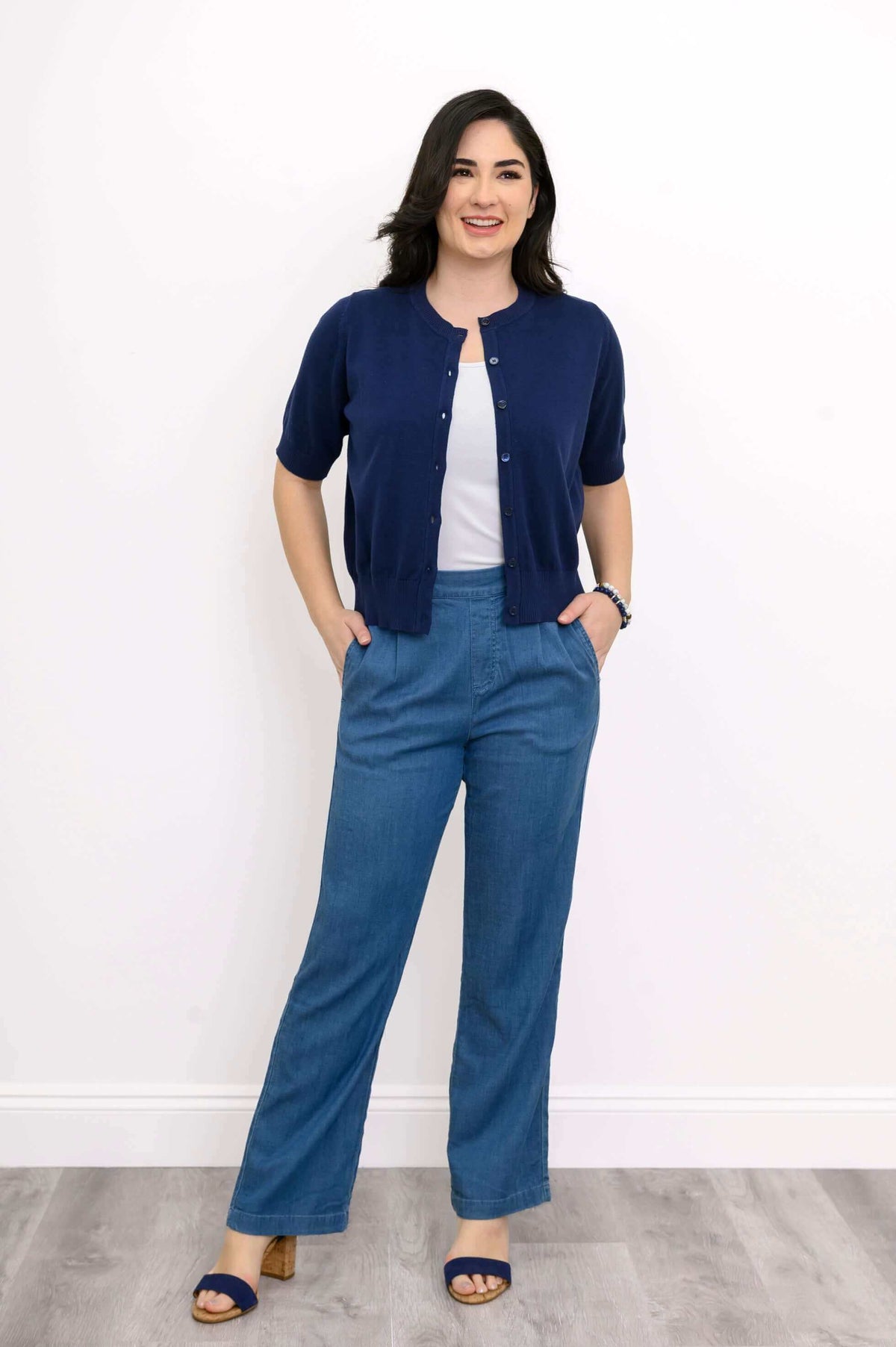 Model standing in navy short sleeve Shen cardigan unbuttoned at top over white tank and blue pants