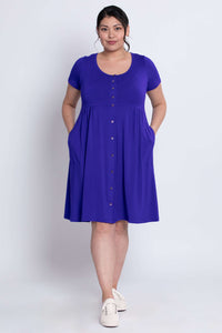 Model showcasing the front of a royal purple empire waist dress with short sleeves and pockets