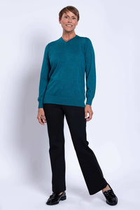 Woman standing in a teal Merino wool V-neck sweater, hands relaxed by her side