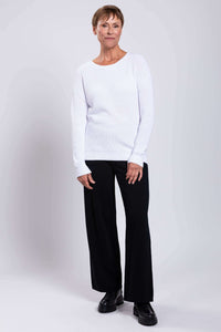 Model standing in a white shaker stitch sweater and black wide-leg pants
