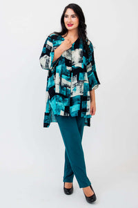 Woman posing hand near collar in Darla blouse and teal pants, studio setting