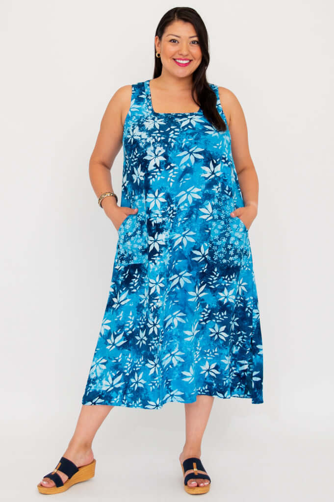 Model in sleeveless blue floral dress, posing with legs apart, square neckline