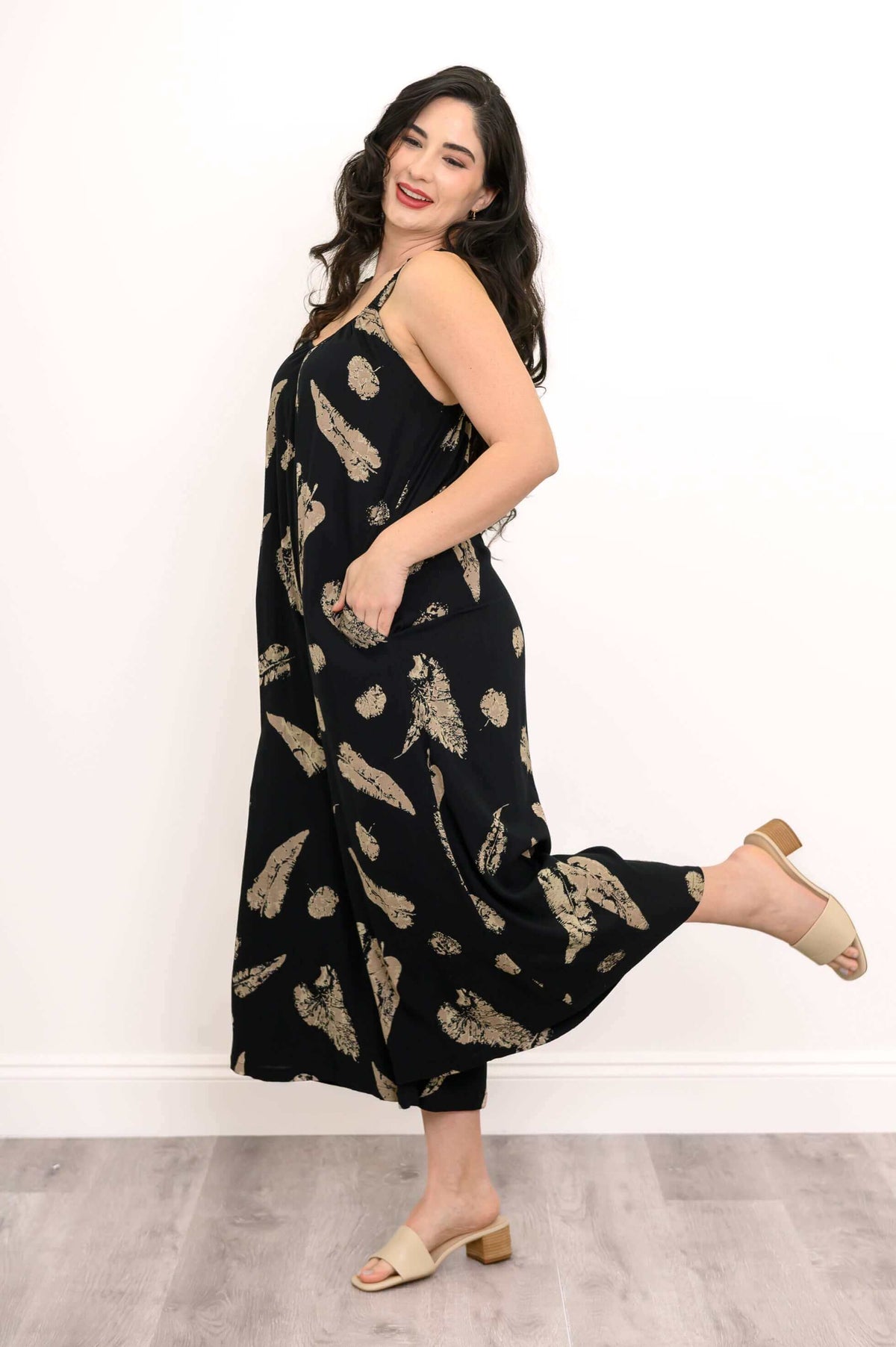 Model in black jumpsuit with tan pattern, leg kicked up playfully