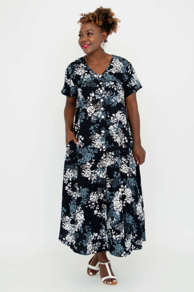 Model posing sideways in a black and white floral dress, one hand in pocket