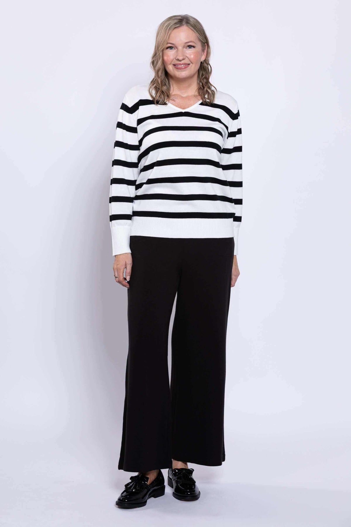 Woman posing in a black and tan Breton stripe V-neck sweater with wide leg pants