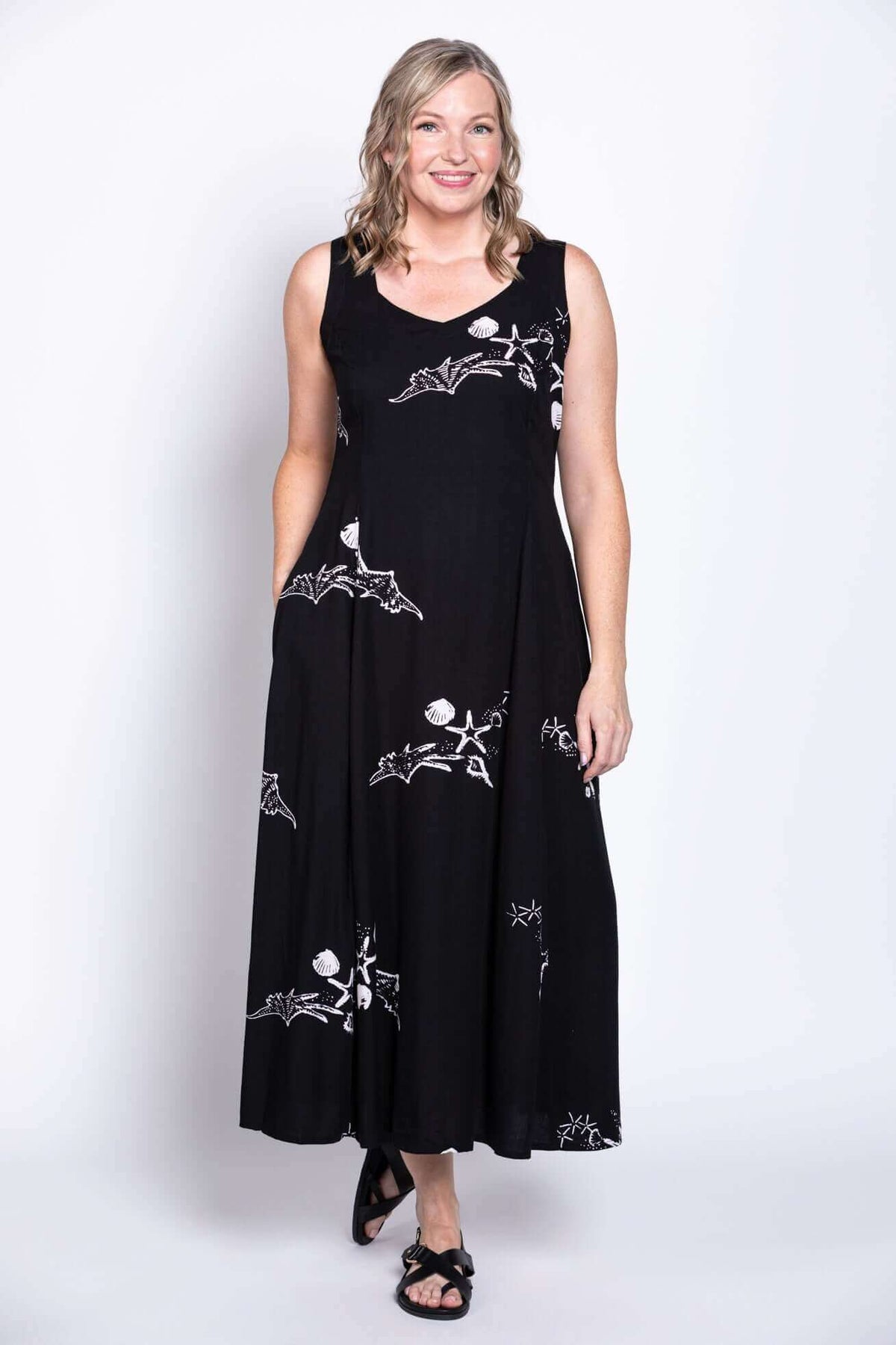 Model in black sleeveless dress with white designs, hands in pockets