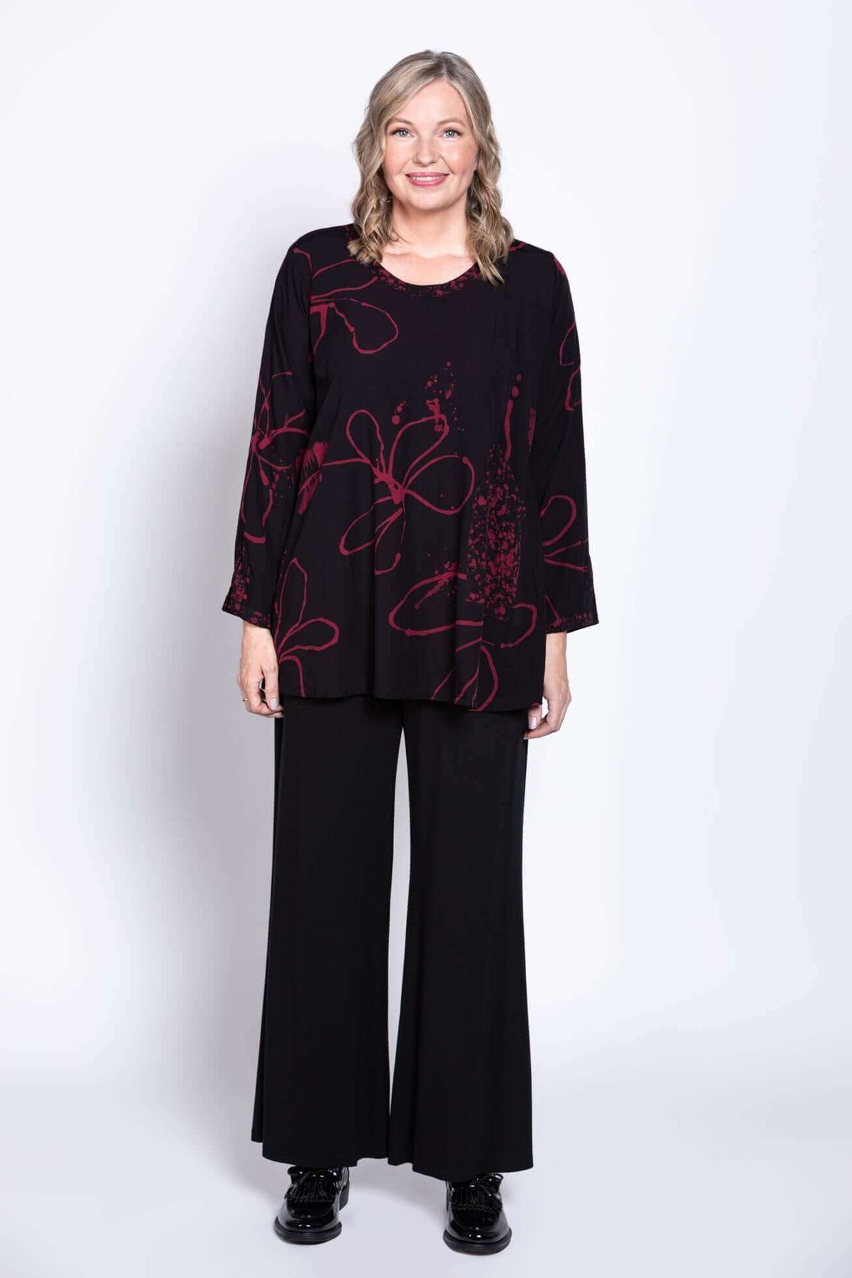 Model smiling in black berry-print blouse and black pants, front view