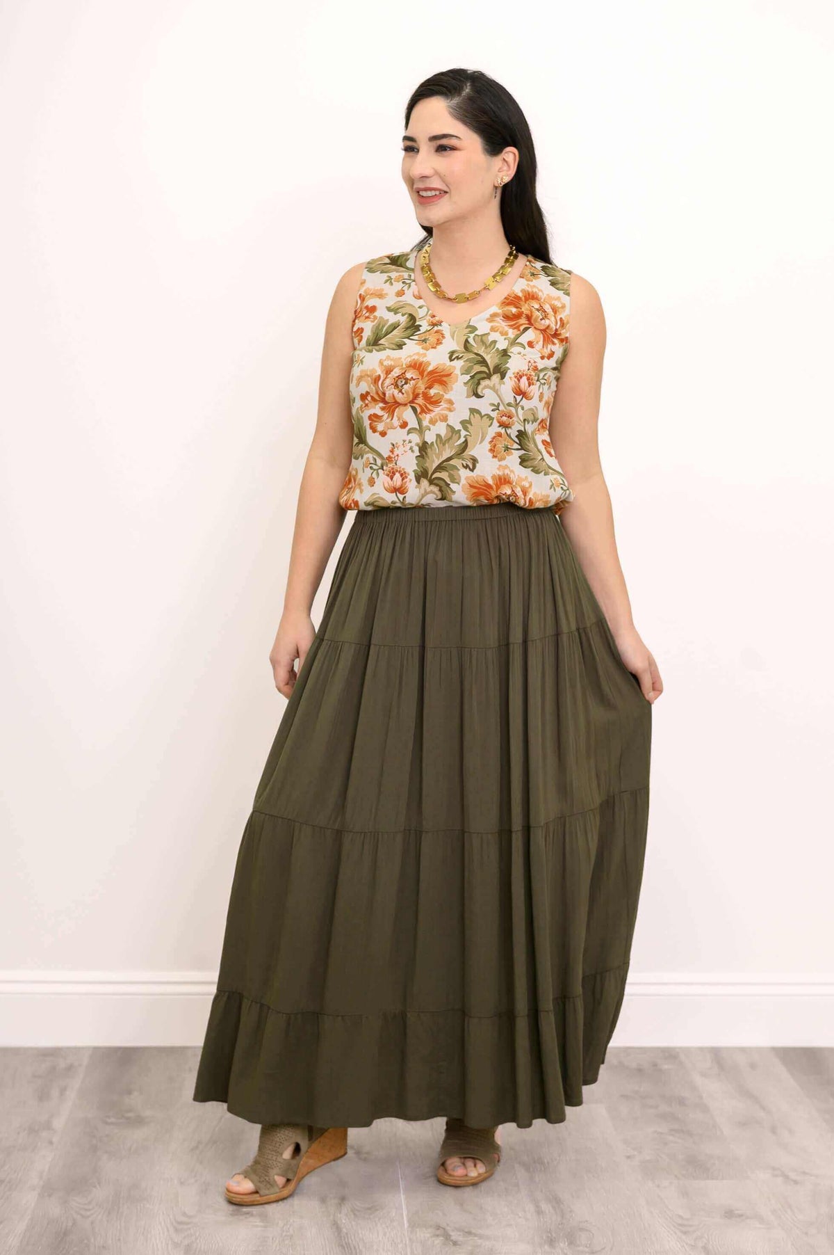 Woman in olive green tiered maxi skirt and floral blouse smiling and holding skirt sides