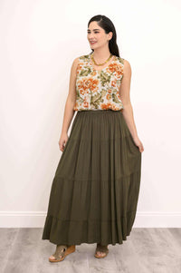 Woman in olive green tiered maxi skirt and floral blouse smiling and holding skirt sides