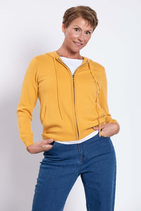 Smiling woman modeling a mustard yellow wool cashmere zip up hoodie with hands in front pockets.