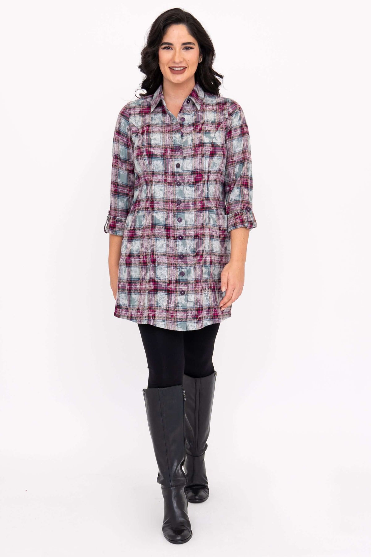 Woman standing wearing a plaid button-up flannel tunic shirt and black boots
