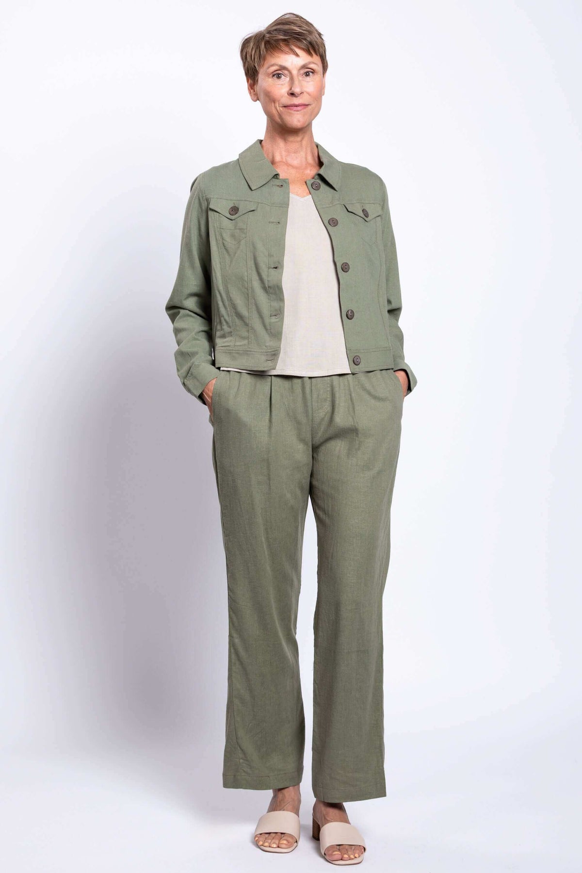 Full body view of model in olive pants and jacket, hands in pockets