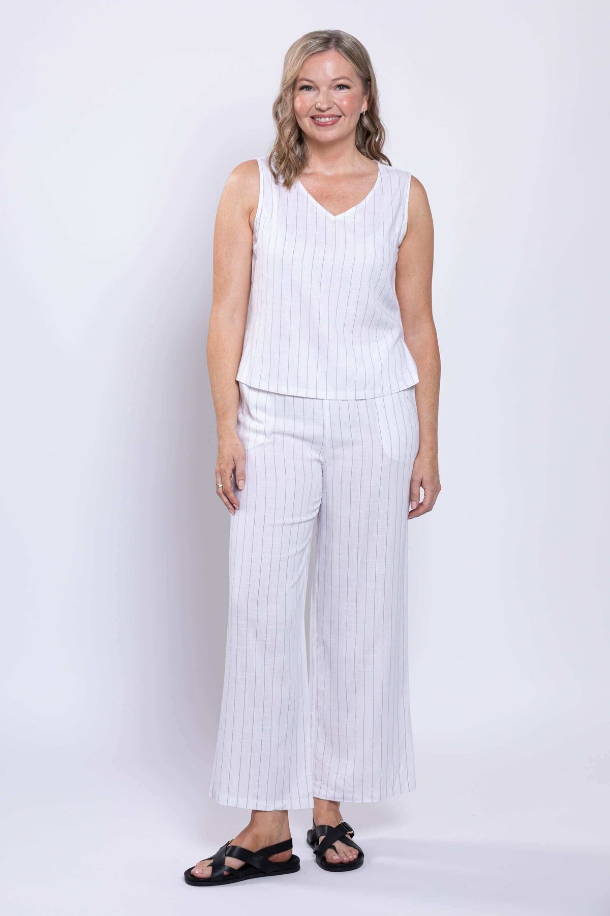 Model standing and smiling in white striped linen-blend tank and matching pants