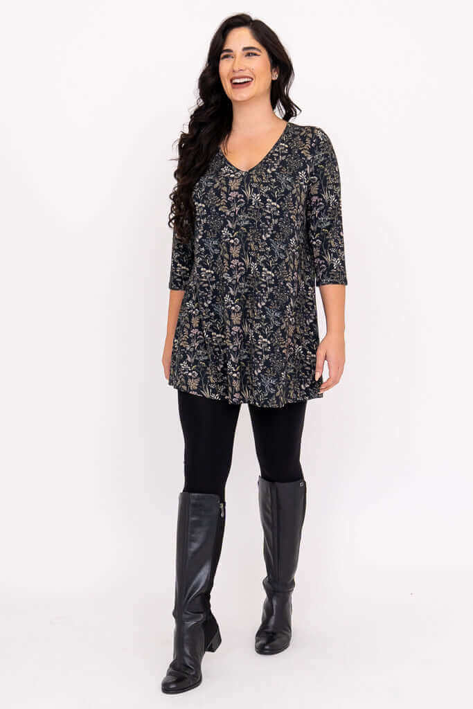 Model smiling and walking in a floral bamboo tunic, black leggings, and boots