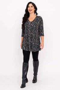 Model smiling and walking in a floral bamboo tunic, black leggings, and boots