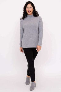 Model walking forward in light grey mock neck sweater, black pants, and grey shoes