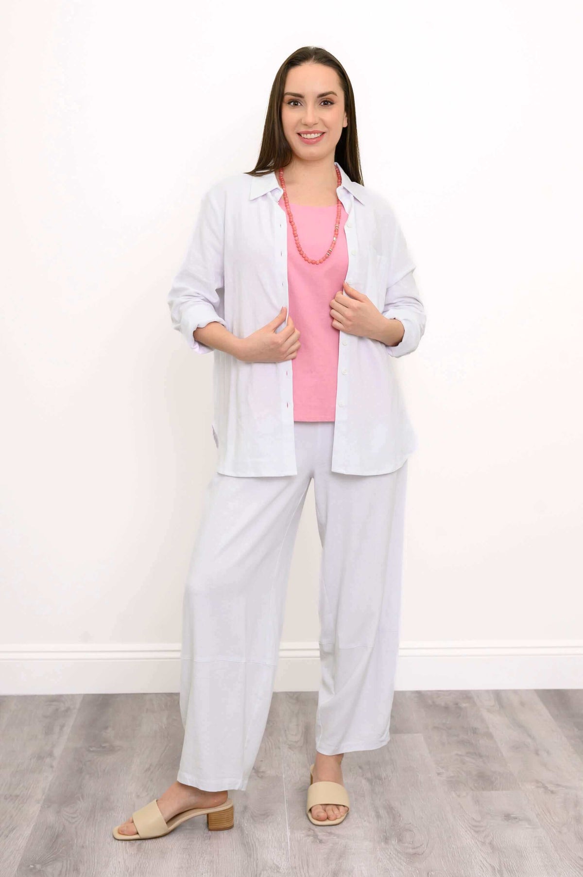Model wearing white shirt on a pink top and white pants, posing with her hands on her shirt
