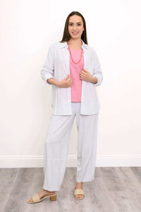 Model wearing white shirt on a pink top and white pants, posing with her hands on her shirt