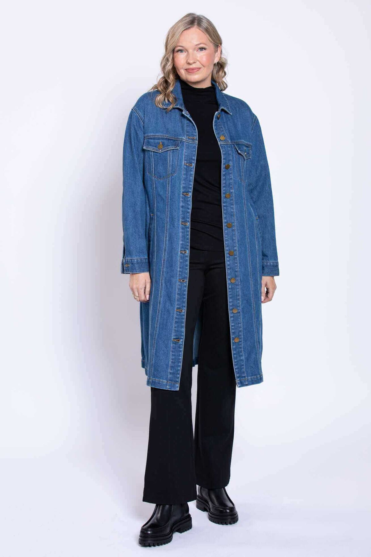Woman modeling longline denim jacket and black boots, front angle