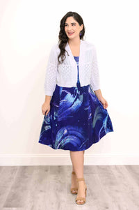 Model wearing blue abstract sleeveless dress layered with a white knit cardigan