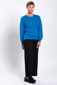 Woman in a blue cable knit sweater, standing with relaxed pose and black loafers