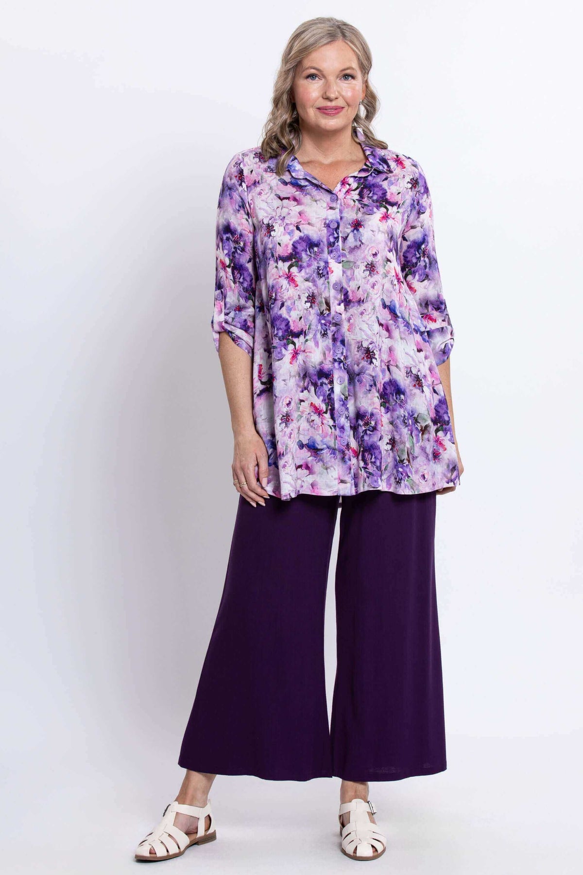 Woman modeling floral tunic top with side seam pockets and purple trousers