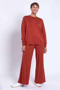 Woman posing in rust bamboo crew neck top and pants set, white background