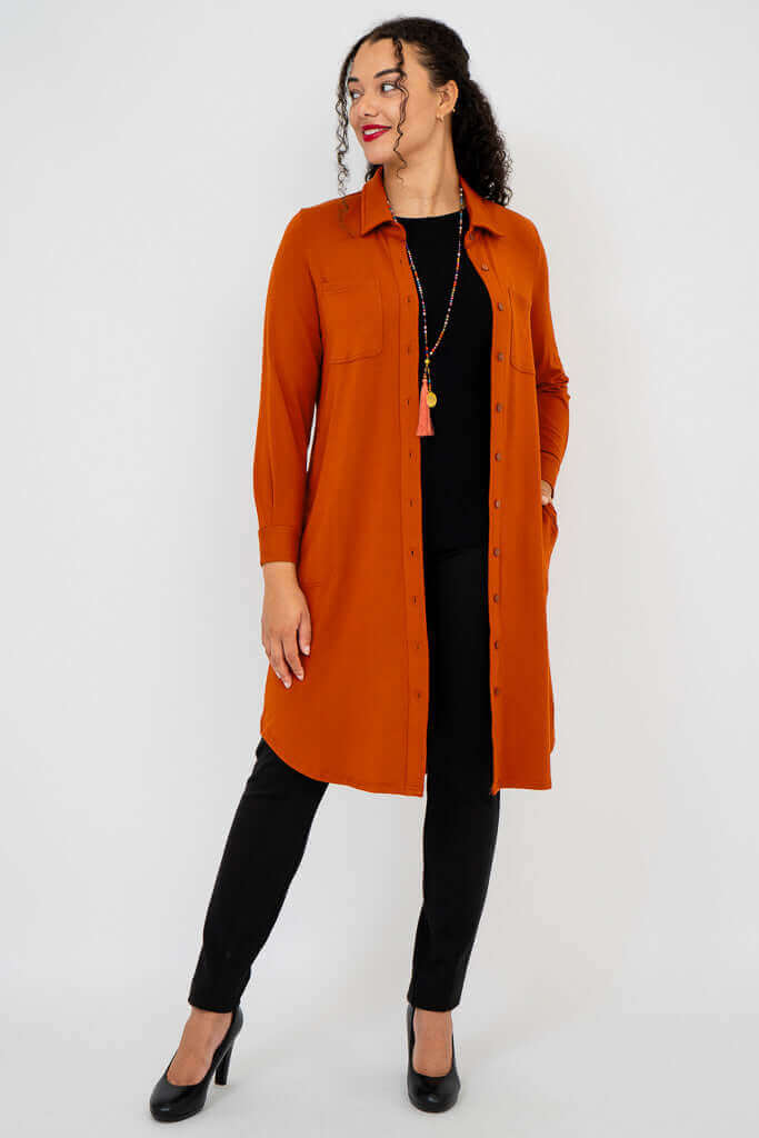 Model wearing rust orange duster shirt with black pants and heels, looking to the side
