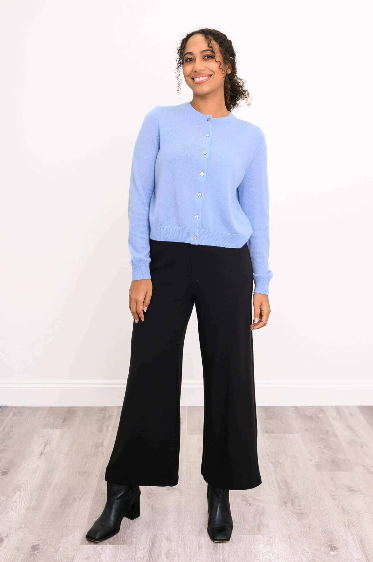 Woman modeling a light blue cashmere cardigan paired with black trousers and heeled boots