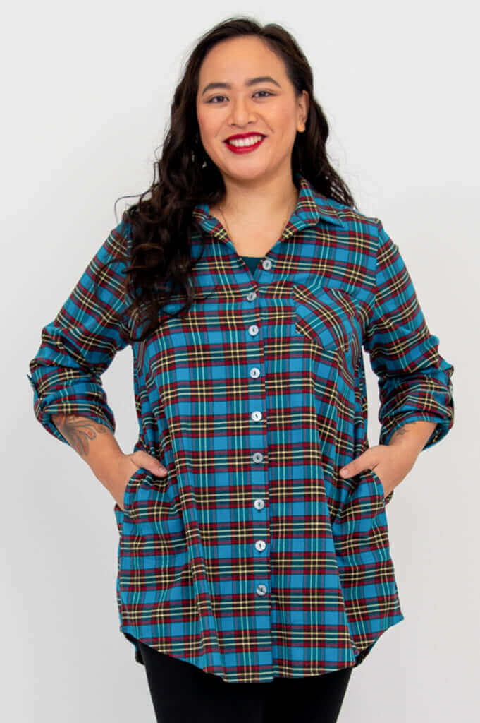Model wears blue plaid flannel tunic buttoned, hands in pockets