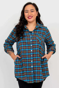 Model wears blue plaid flannel tunic buttoned, hands in pockets