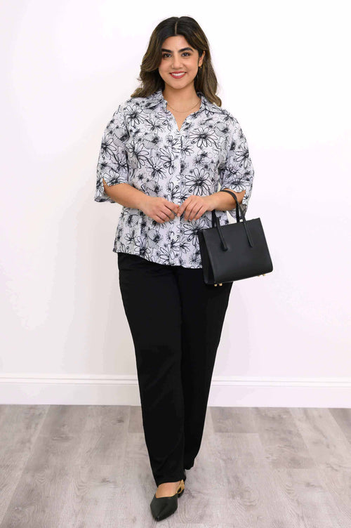 Model holding a black handbag, wearing black and white floral blouse and black pants