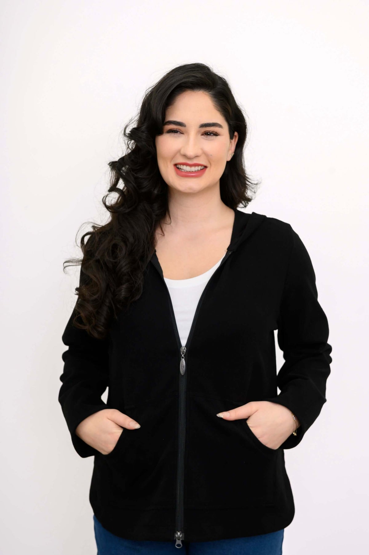 Woman in a black zip hoodie smiling and placing hands in both pockets