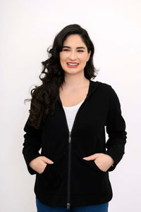 Woman in a black zip hoodie smiling and placing hands in both pockets