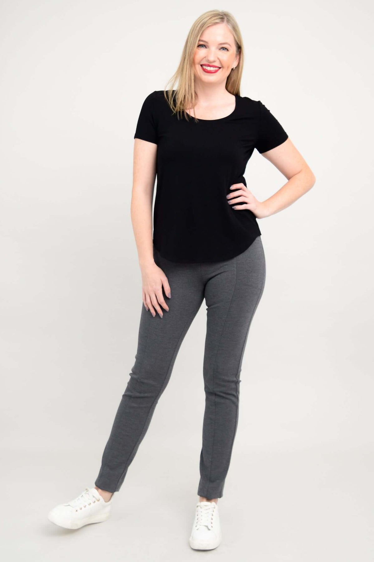 Woman posing with hand on hip in black scoop neck tee and grey pants
