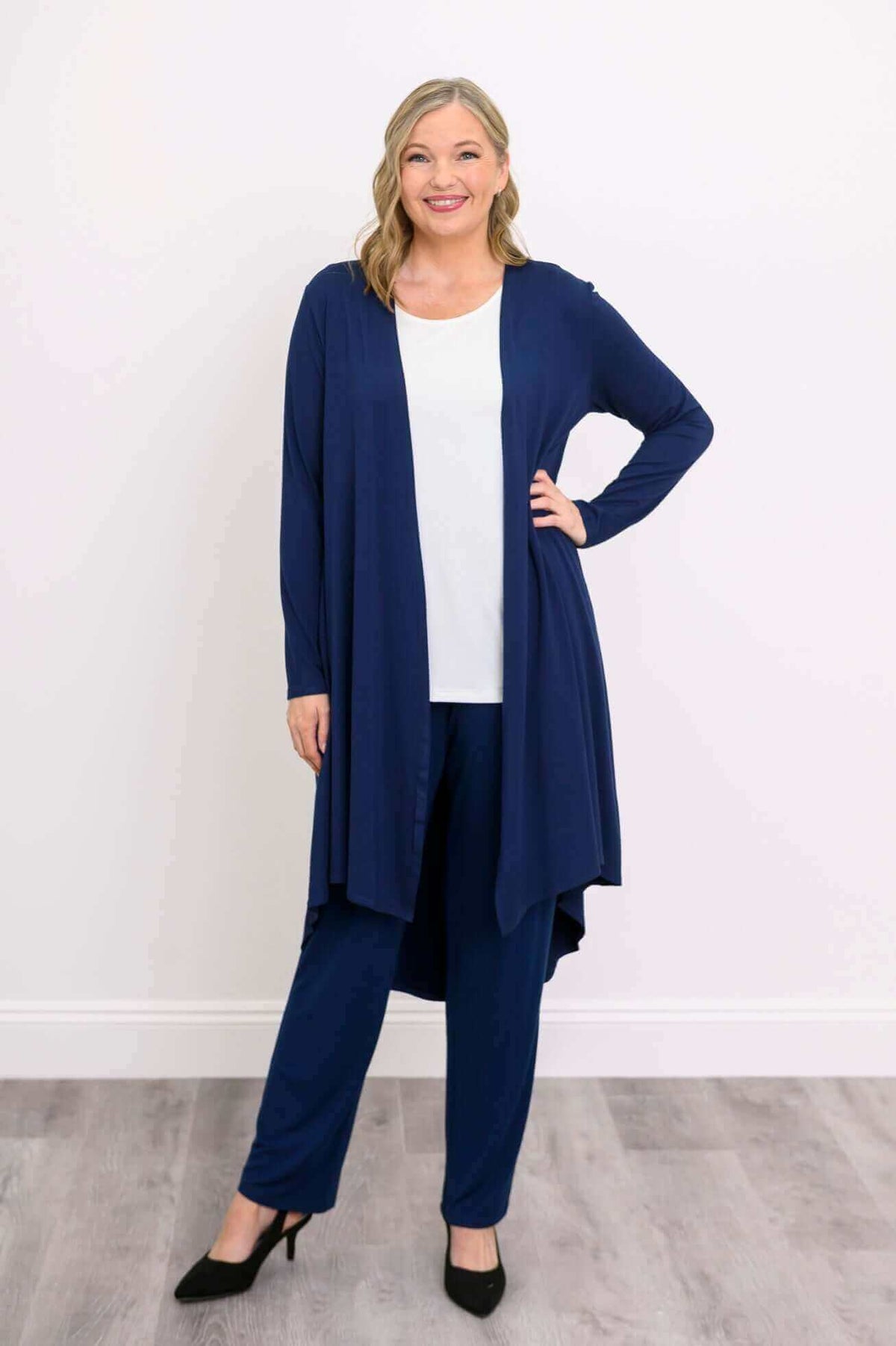 Model posing with hand on hip in navy open front duster layered over white top and blue pants