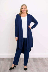 Model posing with hand on hip in navy open front duster layered over white top and blue pants