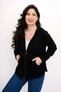 Woman smiling and posing with hands in front pockets of a black zip hoodie