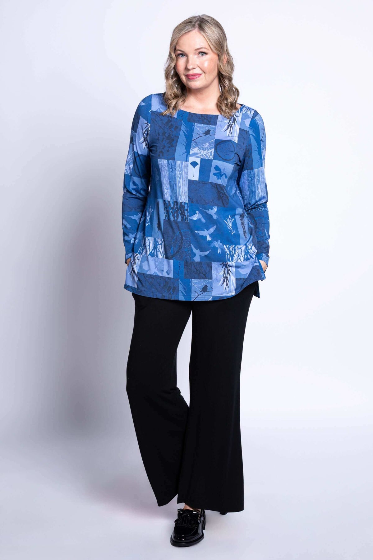 Model with hands in pockets wearing blue patchwork tunic, standing sideways