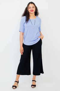 Model with hand in pocket, wearing light blue blouse and black pants